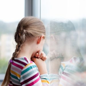Trauriges Kind schaut aus dem Fenster des Heimes